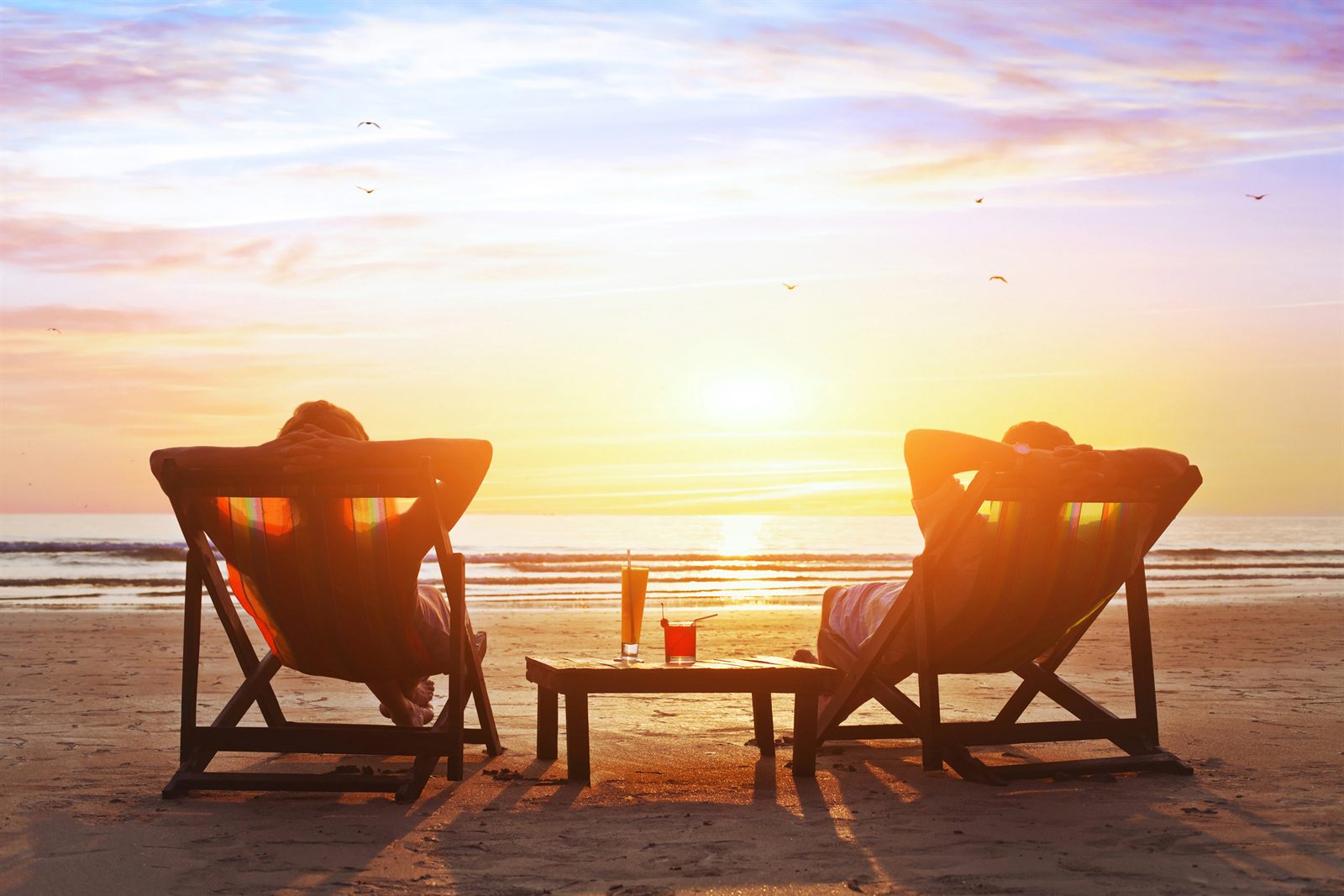 Two people relaxing in deck chairs at sunset by the sea